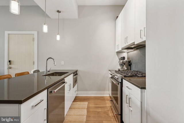 kitchen featuring a sink, white cabinets, hanging light fixtures, appliances with stainless steel finishes, and dark countertops