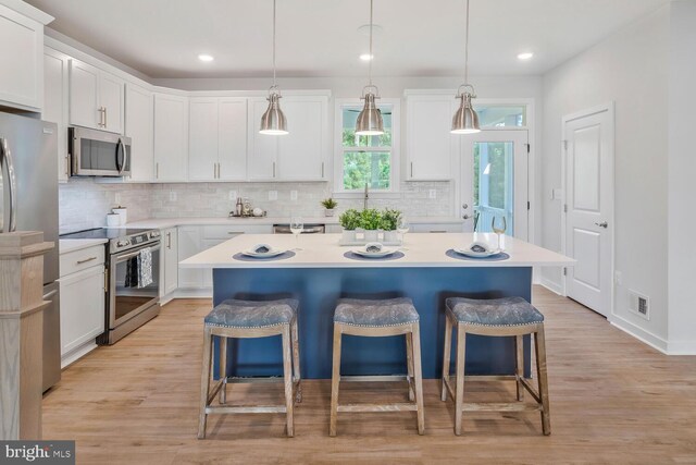 kitchen featuring a kitchen island, white cabinetry, appliances with stainless steel finishes, light hardwood / wood-style floors, and decorative light fixtures