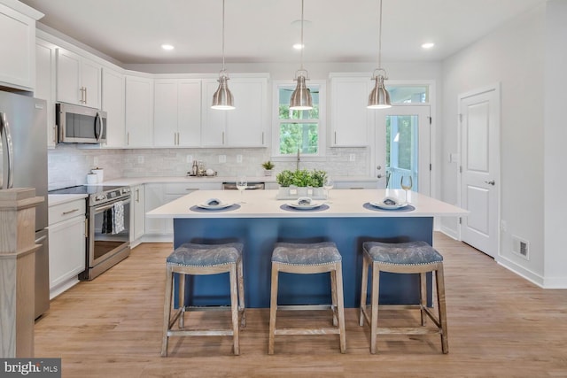 kitchen featuring decorative light fixtures, stainless steel appliances, white cabinets, and a center island with sink