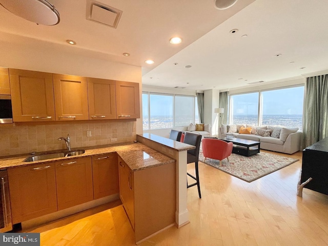 kitchen featuring stone counters, kitchen peninsula, sink, a breakfast bar, and light hardwood / wood-style floors