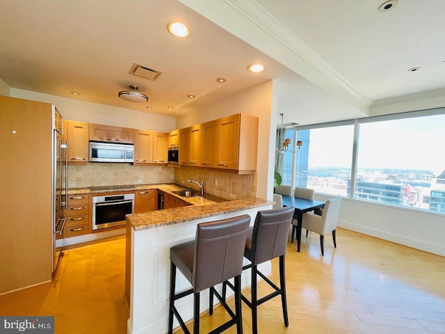 kitchen featuring a kitchen breakfast bar, appliances with stainless steel finishes, light hardwood / wood-style floors, kitchen peninsula, and ornamental molding