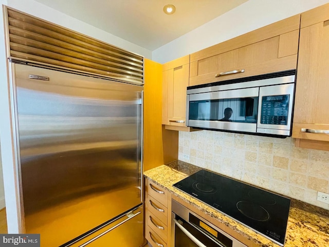 kitchen featuring appliances with stainless steel finishes, decorative backsplash, dark stone counters, and light brown cabinetry