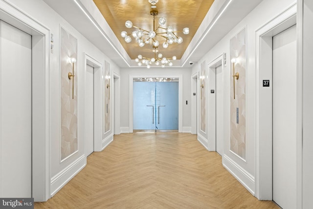 hall with a notable chandelier, elevator, a tray ceiling, and light parquet flooring