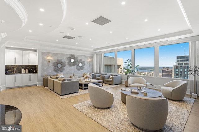 living room featuring light wood-type flooring, a raised ceiling, and ornamental molding