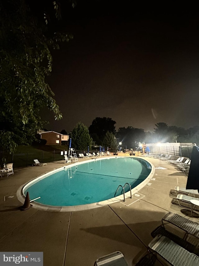 pool at night with a patio, fence, and a community pool