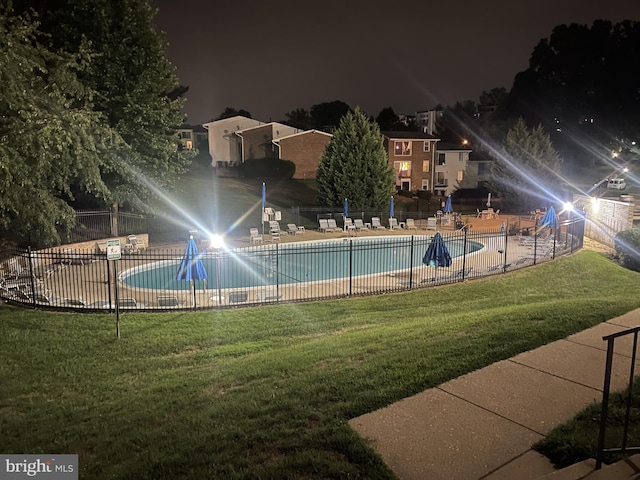 pool at twilight featuring a community pool, fence, and a lawn