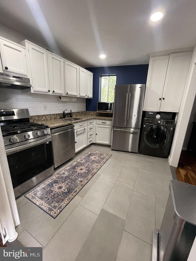 kitchen featuring under cabinet range hood, a sink, white cabinetry, appliances with stainless steel finishes, and washer / dryer