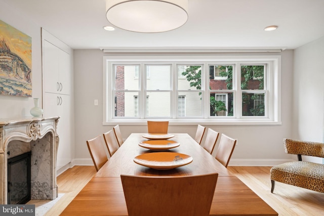 dining room with light wood-type flooring, a premium fireplace, and a wealth of natural light