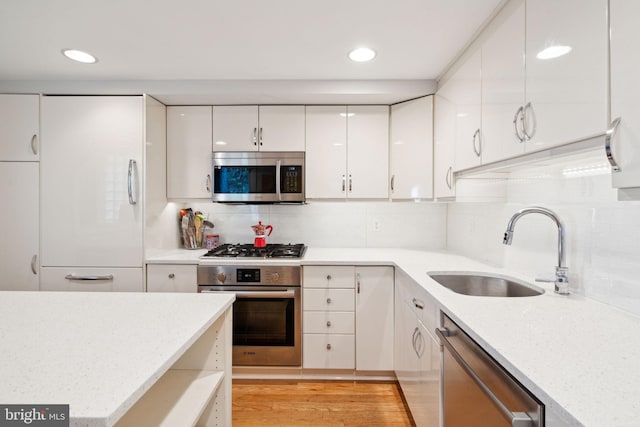 kitchen with sink, backsplash, white cabinetry, appliances with stainless steel finishes, and light hardwood / wood-style floors