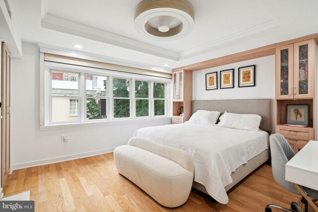 bedroom with ornamental molding, a tray ceiling, and light hardwood / wood-style flooring