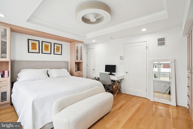 bedroom with ornamental molding, light wood-type flooring, and a raised ceiling