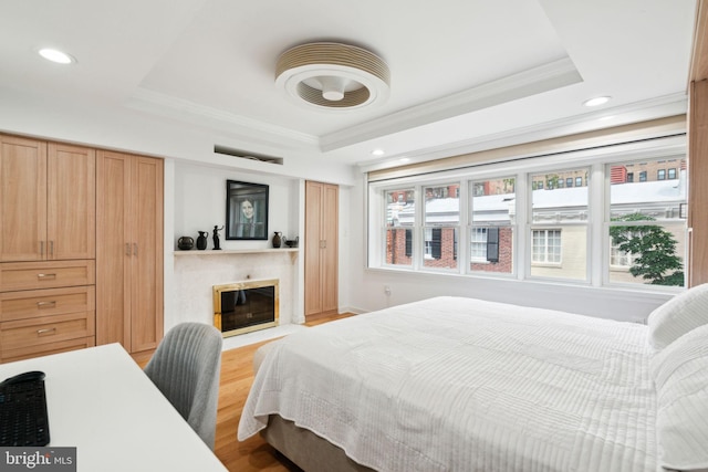 bedroom featuring ornamental molding, a tray ceiling, and light hardwood / wood-style flooring