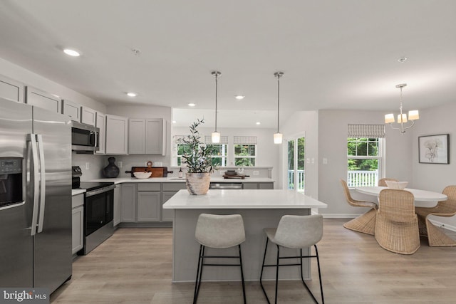 kitchen featuring stainless steel appliances, decorative light fixtures, gray cabinets, and light wood-type flooring