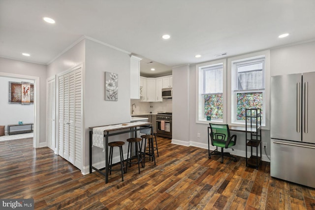 kitchen with appliances with stainless steel finishes, a breakfast bar, dark wood-type flooring, and white cabinets