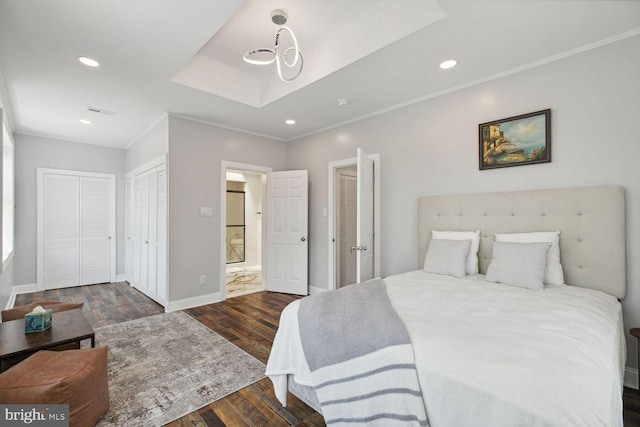 bedroom featuring a raised ceiling, crown molding, dark wood-type flooring, and multiple closets