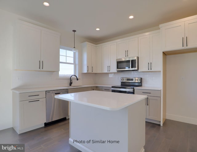 kitchen with a kitchen island, a sink, light countertops, appliances with stainless steel finishes, and pendant lighting