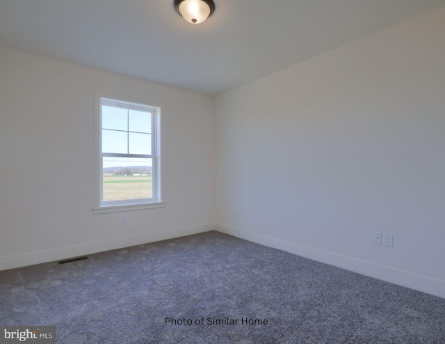 spare room featuring dark colored carpet, visible vents, and baseboards