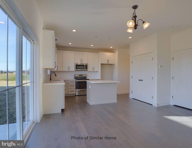 kitchen featuring a kitchen island, hanging light fixtures, hardwood / wood-style floors, white cabinetry, and appliances with stainless steel finishes