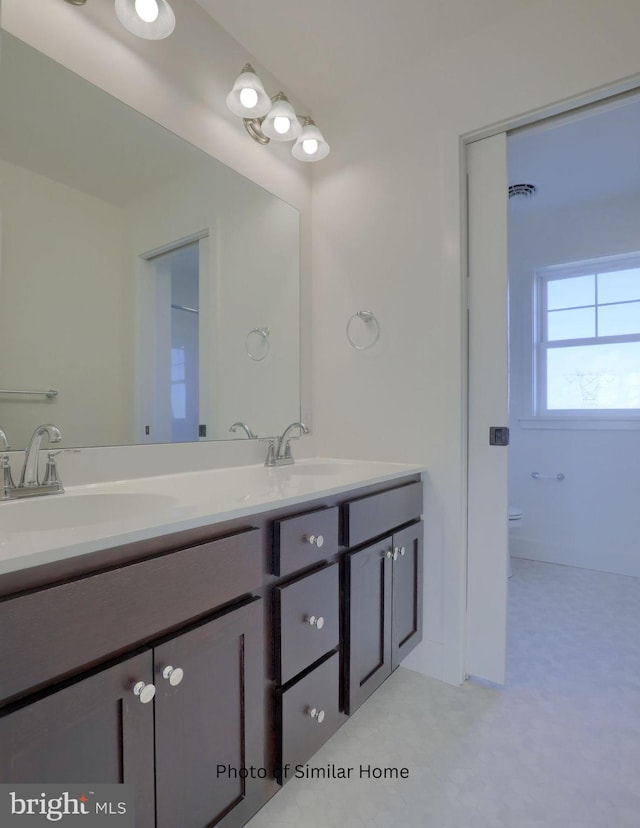 full bath with toilet, double vanity, and a sink