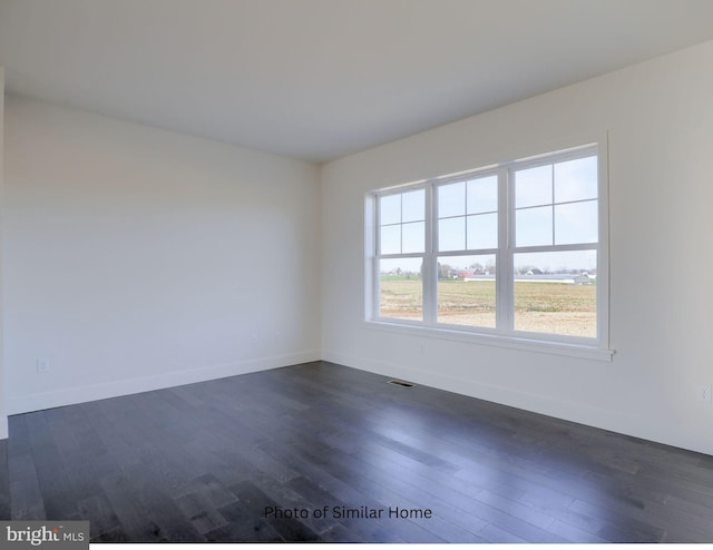 empty room with dark wood-style flooring, visible vents, and baseboards