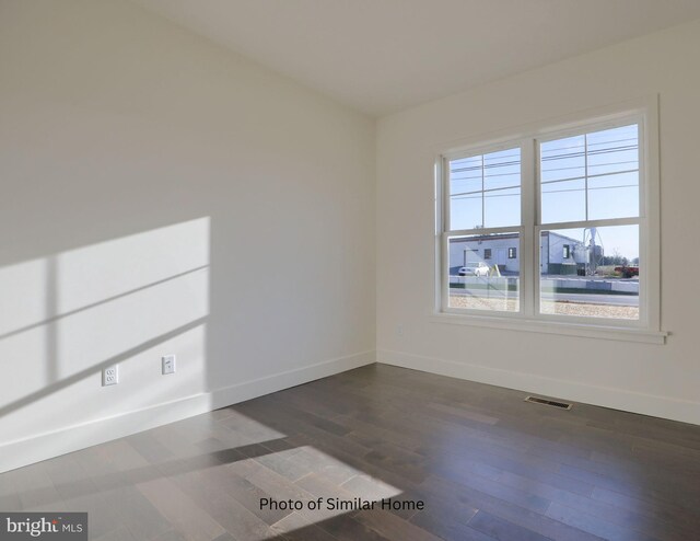 spare room with dark wood-style flooring, visible vents, and baseboards