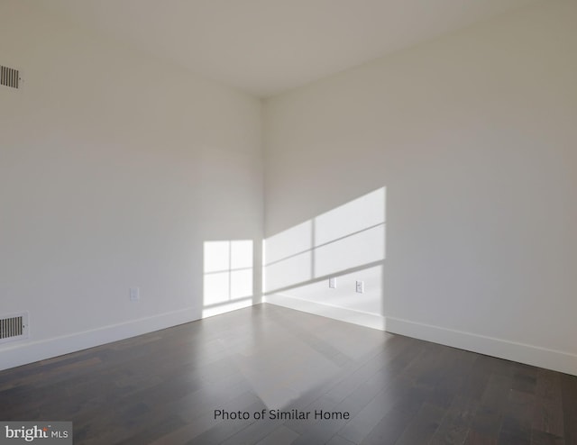 empty room with dark wood-style floors, visible vents, and baseboards