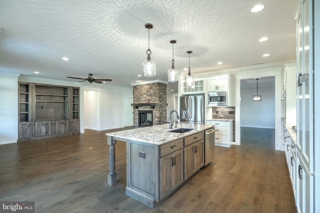 kitchen with a stone fireplace, dark hardwood / wood-style flooring, appliances with stainless steel finishes, a kitchen island with sink, and white cabinetry