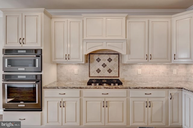 kitchen with backsplash, stainless steel double oven, and light stone counters