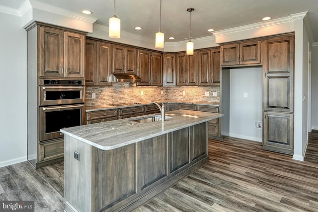 kitchen with stainless steel double oven, decorative backsplash, light stone countertops, an island with sink, and dark hardwood / wood-style floors