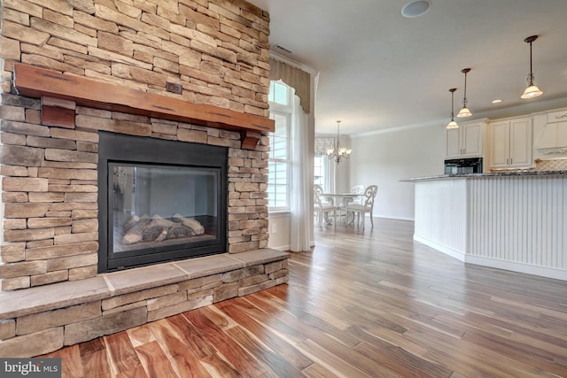 unfurnished living room featuring hardwood / wood-style flooring, crown molding, a notable chandelier, and a fireplace