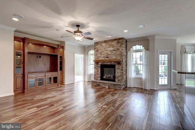 unfurnished living room with ceiling fan, hardwood / wood-style flooring, a stone fireplace, and ornamental molding