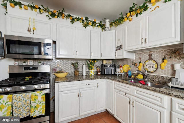 kitchen featuring white cabinets, decorative backsplash, dark stone countertops, and stainless steel appliances