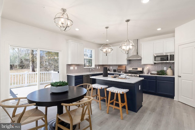 kitchen featuring wall chimney range hood, decorative light fixtures, light wood-type flooring, and stainless steel appliances