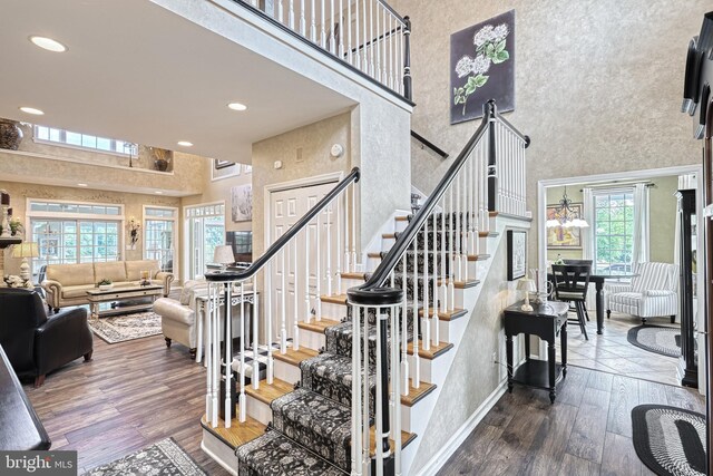 stairs with recessed lighting, wood finished floors, a towering ceiling, and baseboards