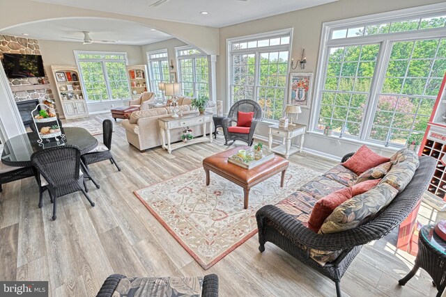 living room with ceiling fan, arched walkways, a stone fireplace, baseboards, and light wood-style floors