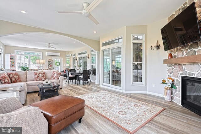 living area with arched walkways, ceiling fan, a fireplace, wood finished floors, and a wall mounted air conditioner