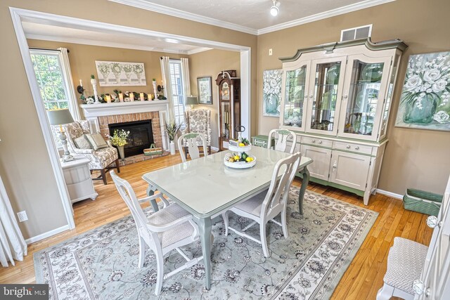 dining space with light wood-style floors, a brick fireplace, visible vents, and crown molding