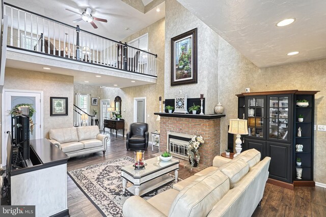 living room with stairs, a brick fireplace, dark wood finished floors, and a ceiling fan