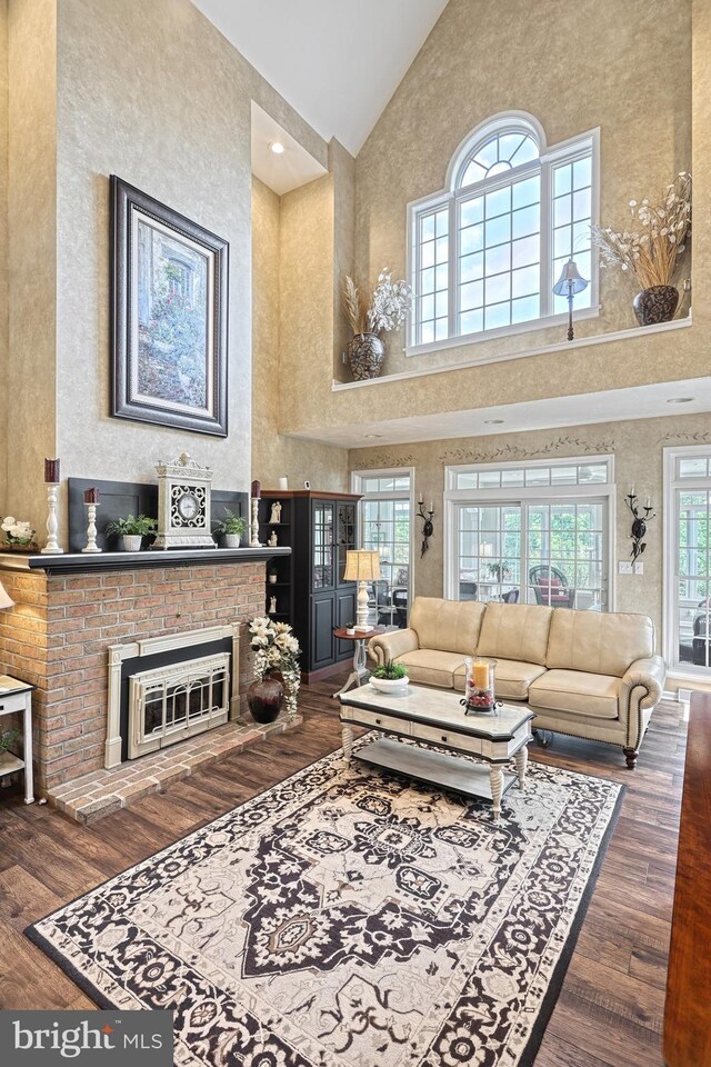 living area with high vaulted ceiling, a brick fireplace, and wood finished floors