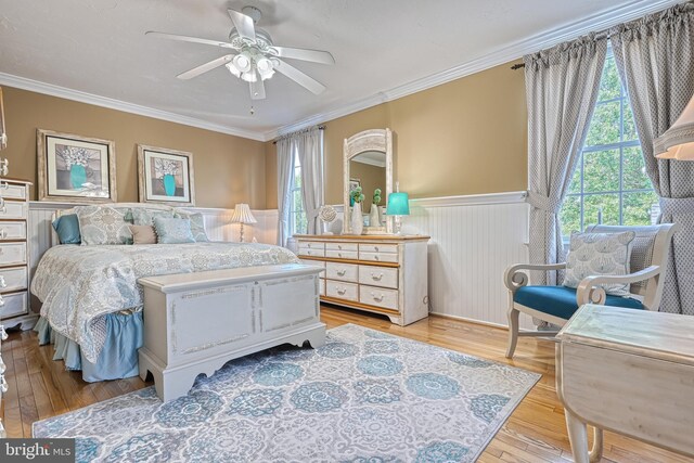 bedroom featuring multiple windows, wainscoting, light wood-style flooring, and crown molding