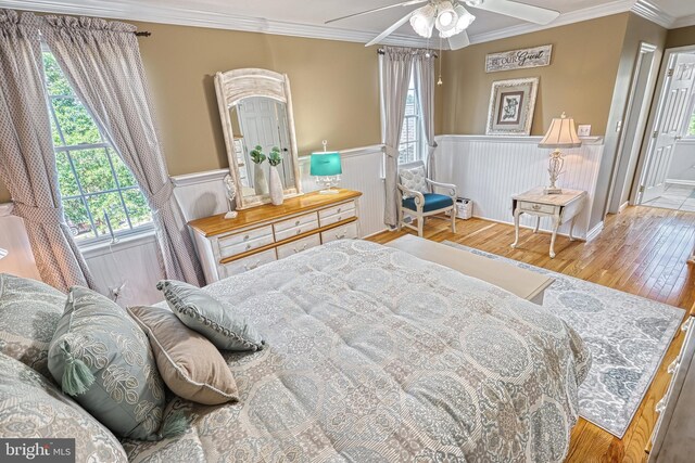 bedroom featuring light wood-type flooring, a wainscoted wall, and crown molding