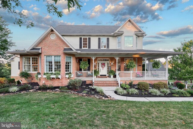 view of front facade with a shingled roof, a front yard, covered porch, and brick siding