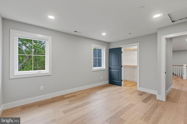 unfurnished bedroom featuring a closet, a walk in closet, and light wood-type flooring