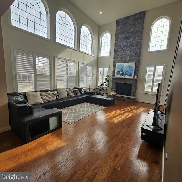 living room featuring a fireplace, a high ceiling, wood-type flooring, and a healthy amount of sunlight