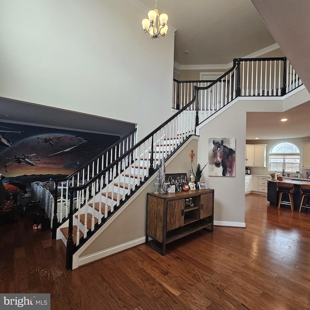 staircase with a high ceiling, ornamental molding, hardwood / wood-style flooring, and a notable chandelier