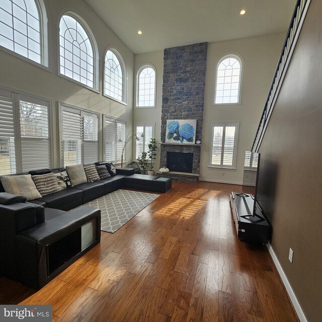 living room with a high ceiling, hardwood / wood-style flooring, and a stone fireplace