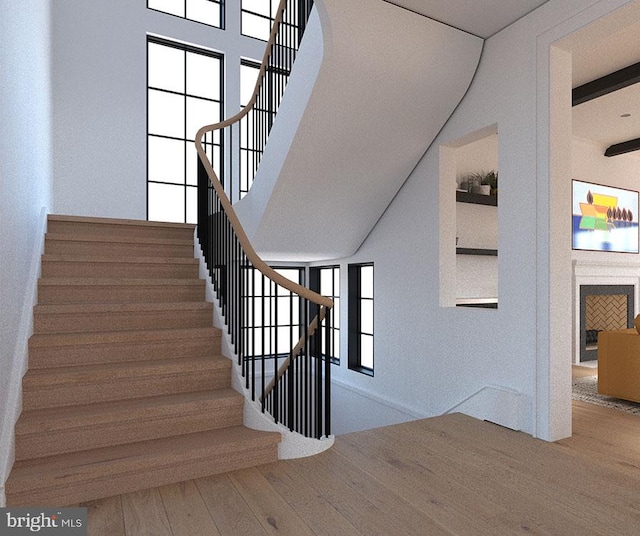 staircase featuring a fireplace, wood finished floors, beam ceiling, and a healthy amount of sunlight