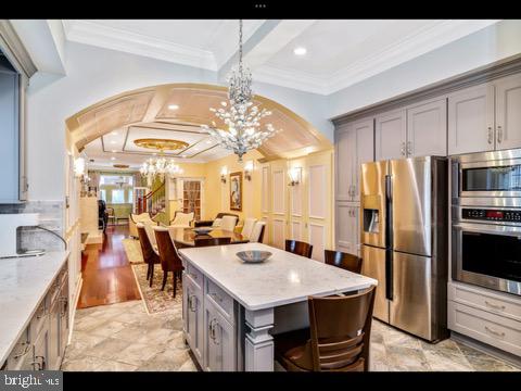 kitchen featuring light tile patterned flooring, appliances with stainless steel finishes, coffered ceiling, a kitchen island, and crown molding