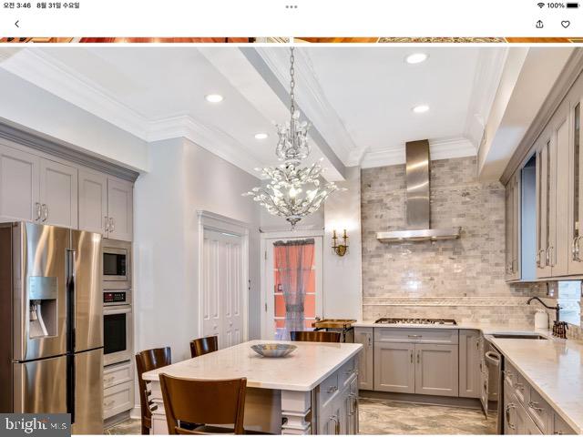 kitchen featuring appliances with stainless steel finishes, a chandelier, wall chimney exhaust hood, sink, and a kitchen island