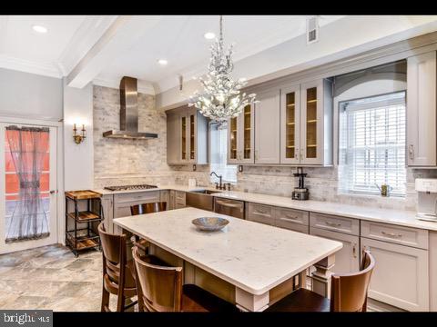 kitchen with wall chimney range hood, decorative backsplash, an inviting chandelier, and light tile patterned floors